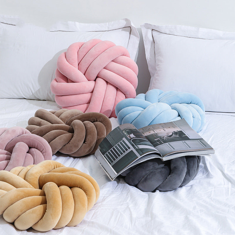 Colorful knotted cushions on a bed with an open magazine.