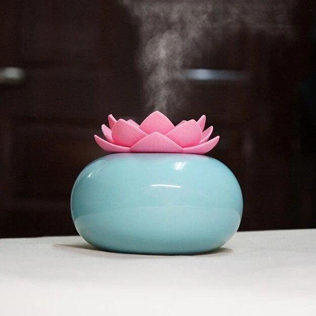 Pink lotus-shaped diffuser on a blue base emitting steam against a dark background