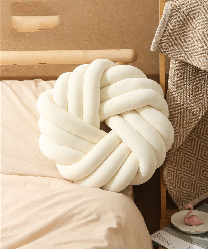 White knot pillow on a bed with a neutral background