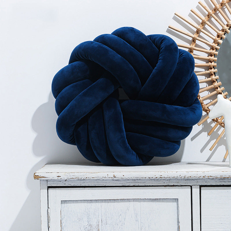 Navy blue knot pillow on a white cabinet with a decorative mirror in the background
